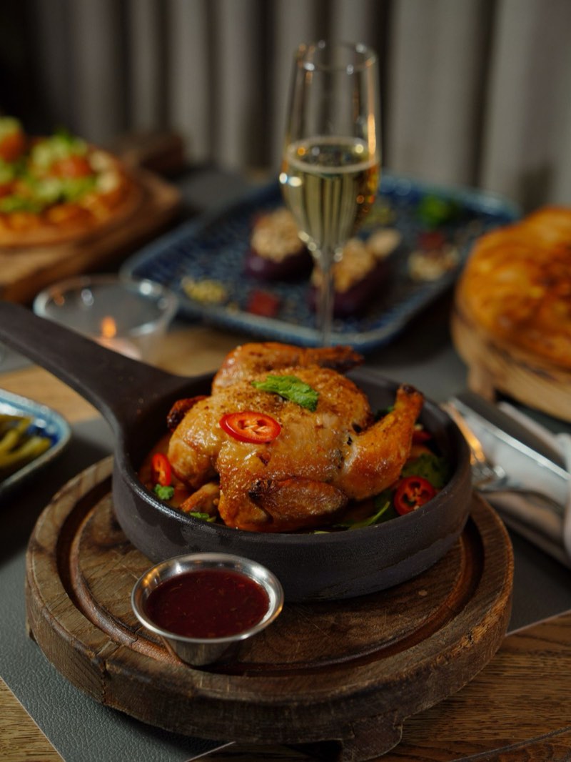 Half chicken in a cast-iron pan, chili and herbs, glass of sparkling wine behind