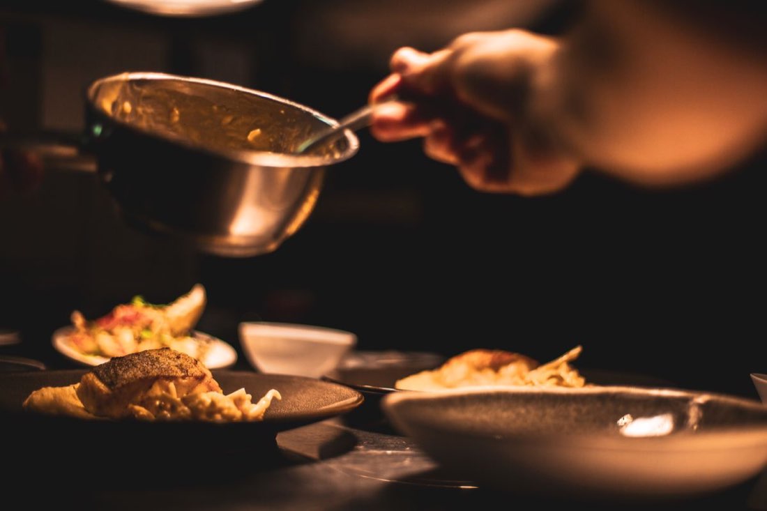 A cook saucing plates in the low light of the pass