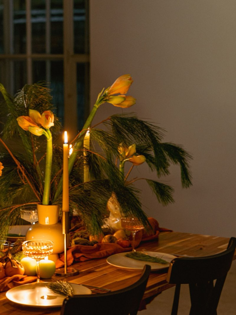 A long table set with taper candles, amaryllis, and persimmons